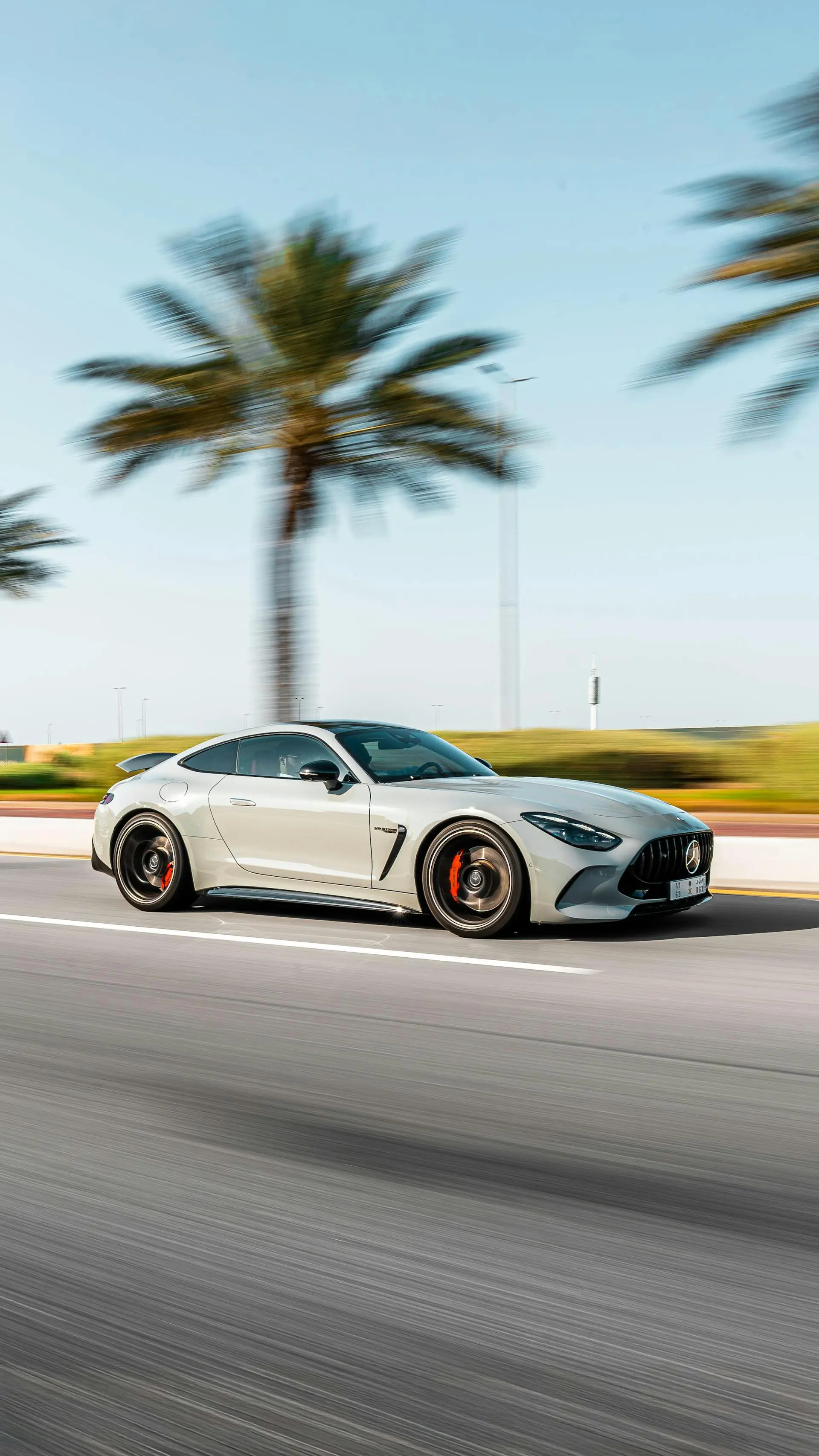 A gray sports car driving at high speed on a road, with blurred palm trees and a clear sky in the background.
