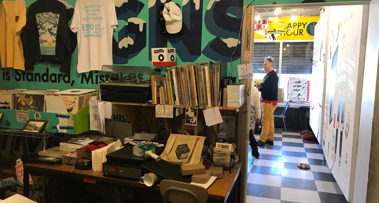 A photo of an art workshop filled with different objects like sketchbooks, printed t-shirts and flyers.