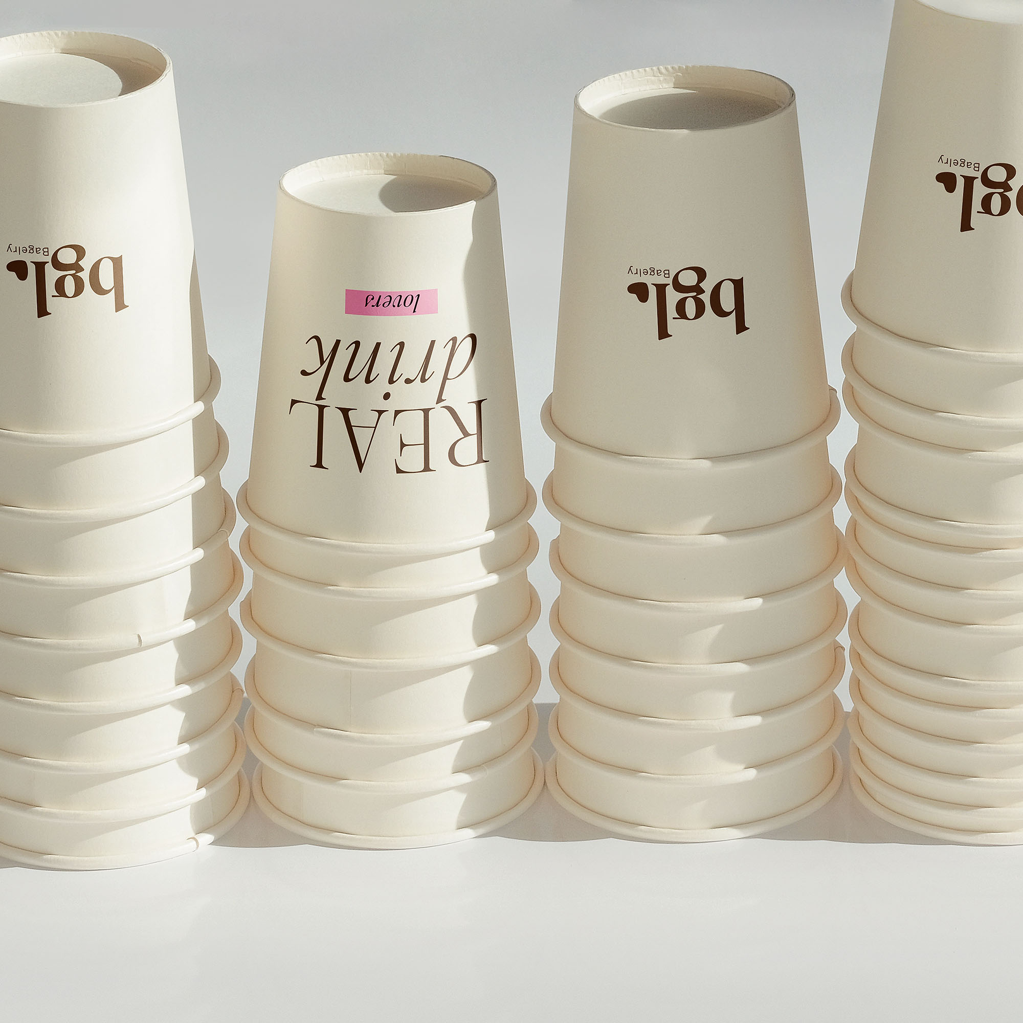 Four stacks of white paper coffee cups, each branded with "bgl." and a pink label reading "REAL drink lovers."