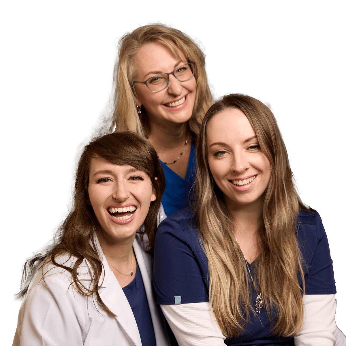 Three smiling women in scrubs pose together, with one in a white coat, showcasing camaraderie in a professional setting.