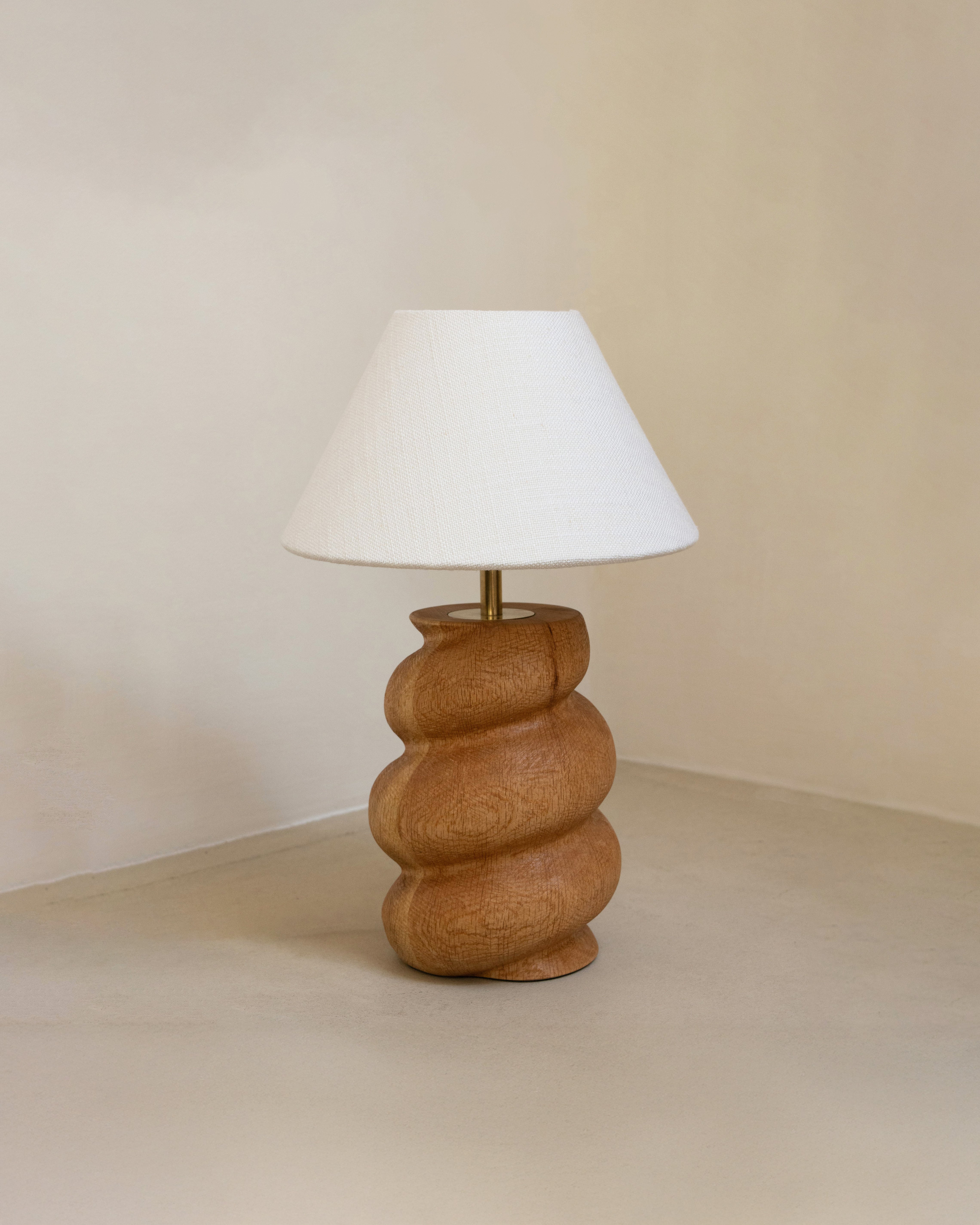 Caracol Table Lamp in oak and white shade on a beige surface.
