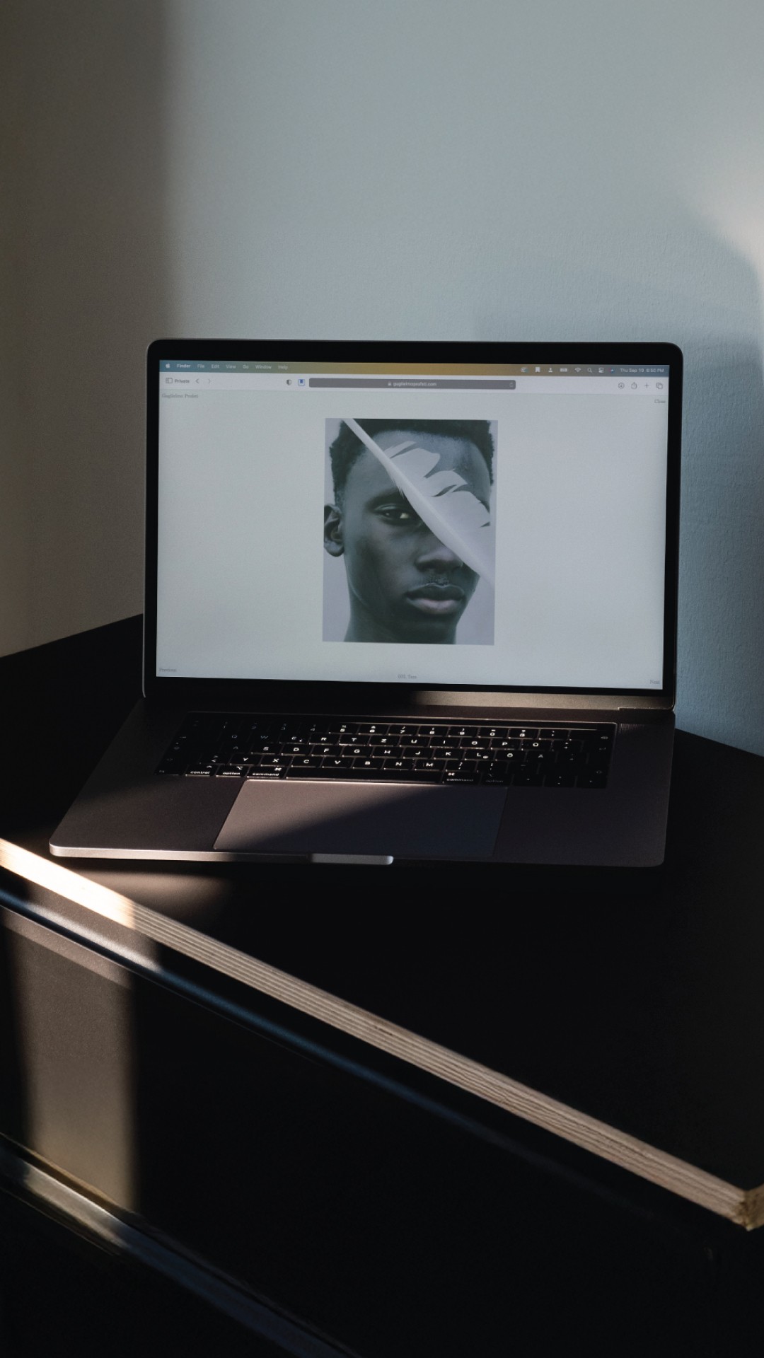 Smiling young woman with long hair standing against a dark green background, holding a finger to her chin.
