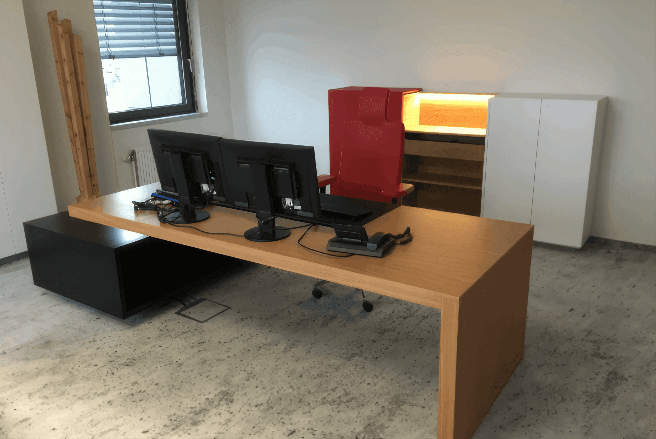 MW Interior - Chefbüro mit großem Eichen-Schreibtisch, Doppelmonitor und rotem Designstuhl" Beschreibung: Repräsentatives Einzelbüro mit ausladendem Holzschreibtisch, Doppelbildschirm-Arbeitsplatz und markant rotem Bürostuhl – ergänzt durch eine beleuchtete Sideboard-Einheit in Weiß.