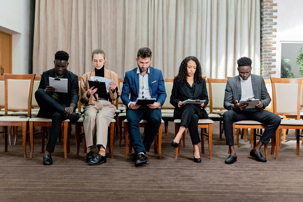 Five diverse job seekers sit in a waiting room reviewing their resumes, reflecting the highly competitive 2026 Canadian job market.