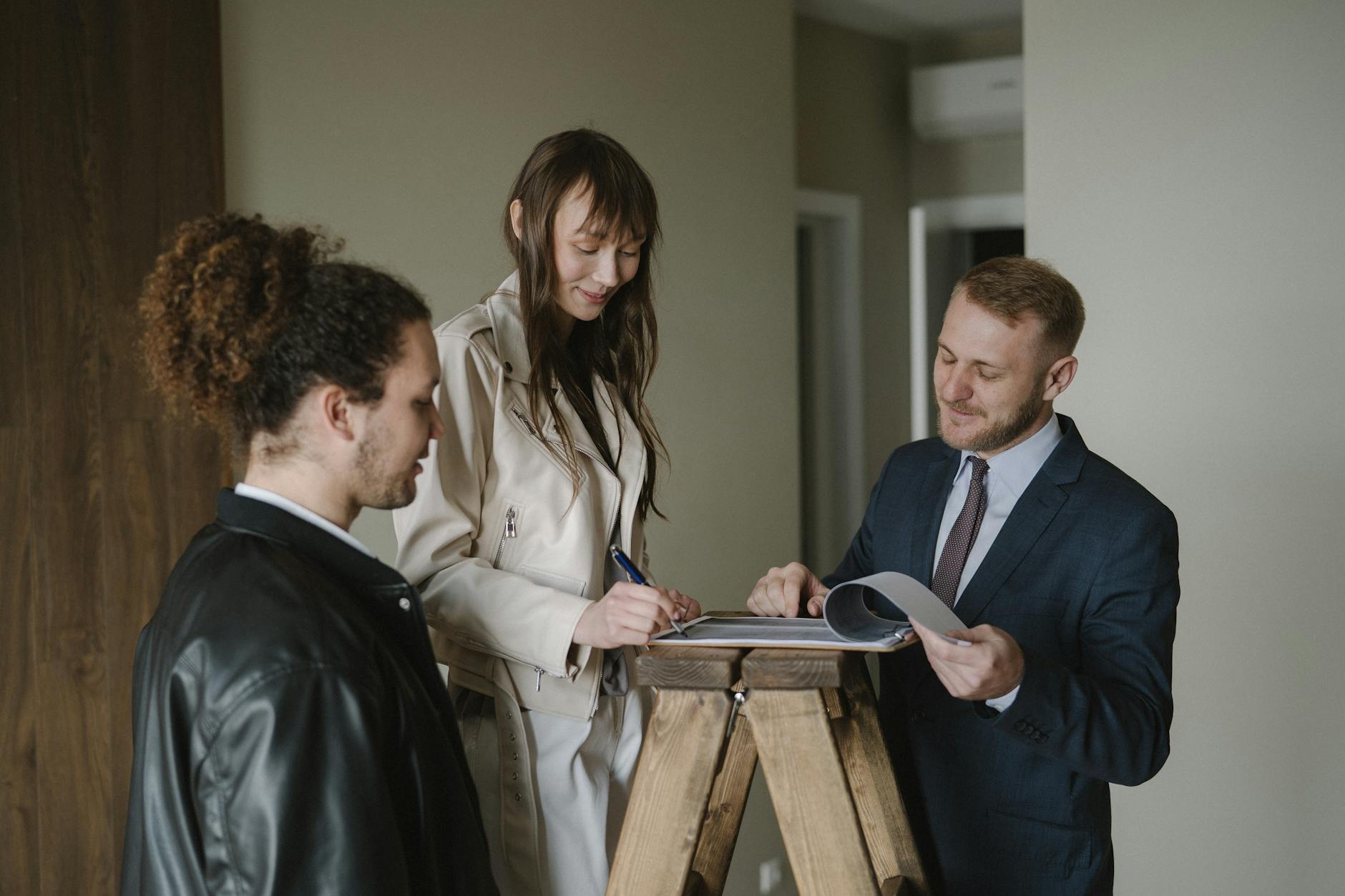 Estate agent with two clients signing property paperwork propped on a wooden stepladder inside a flat