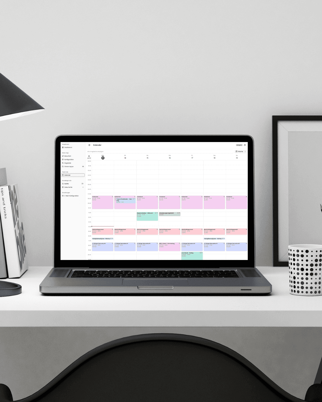 A modern, sleek office setup features a widescreen monitor displaying business analytics dashboards with charts and graphs, next to a closed laptop on a white desk in a bright, minimalist room with light curtains and a potted plant in the corner.