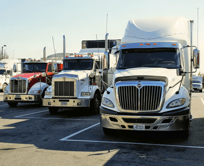 Row of semi-trucks parked in designated spaces at a truck stop.