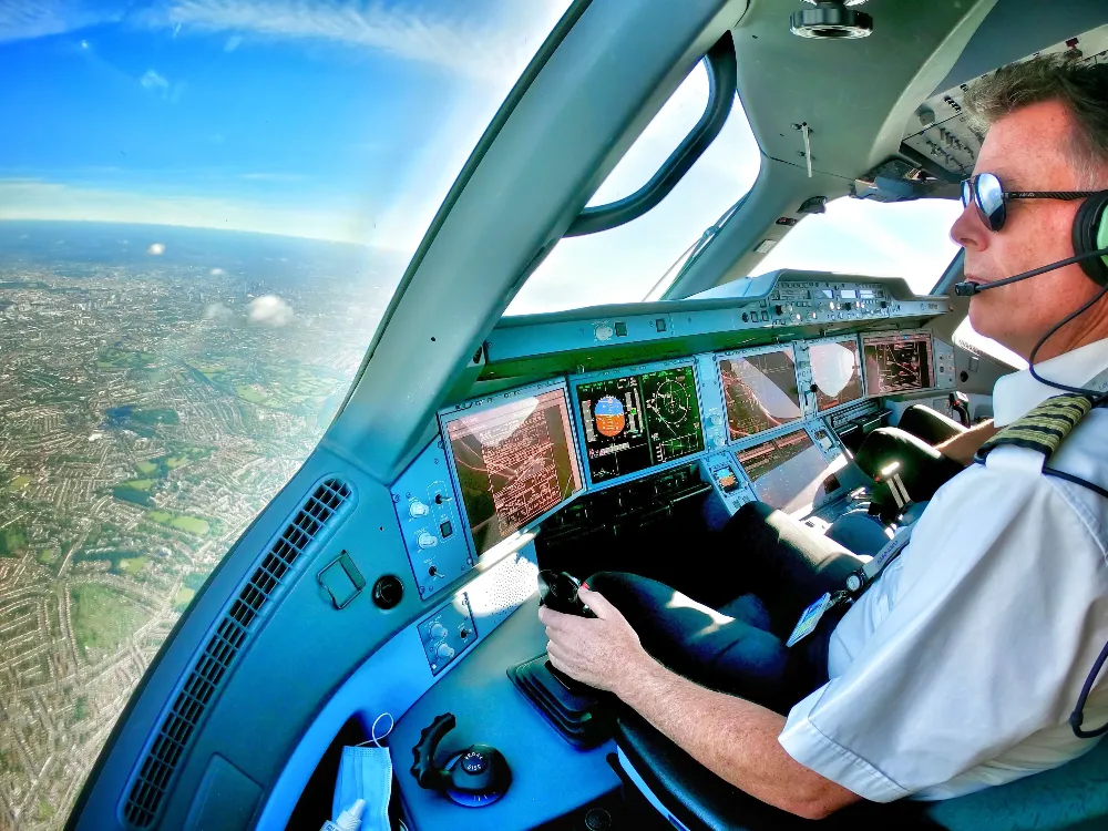 Captain Chris flying a commercial aircraft with cockpit instruments visible and city landscape below.