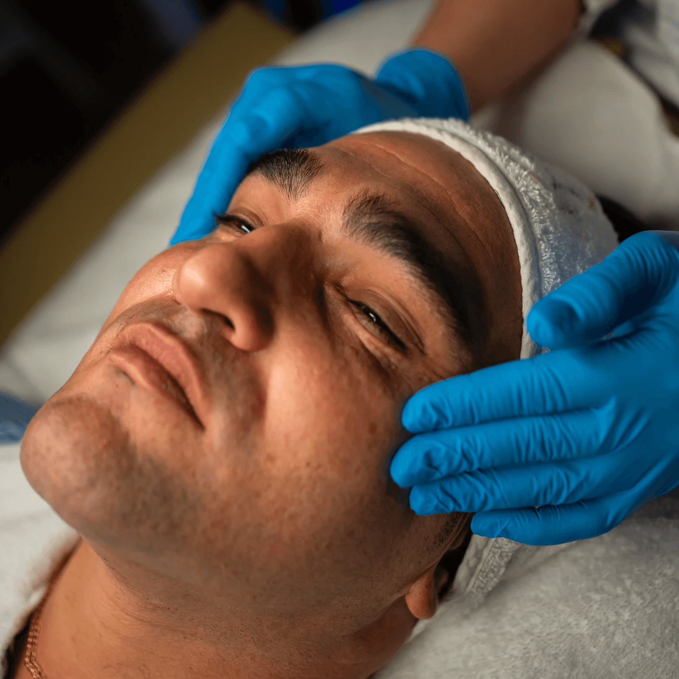 Young woman with a green towel wrapped around her head, wearing under-eye patches and smiling during a self-care routine