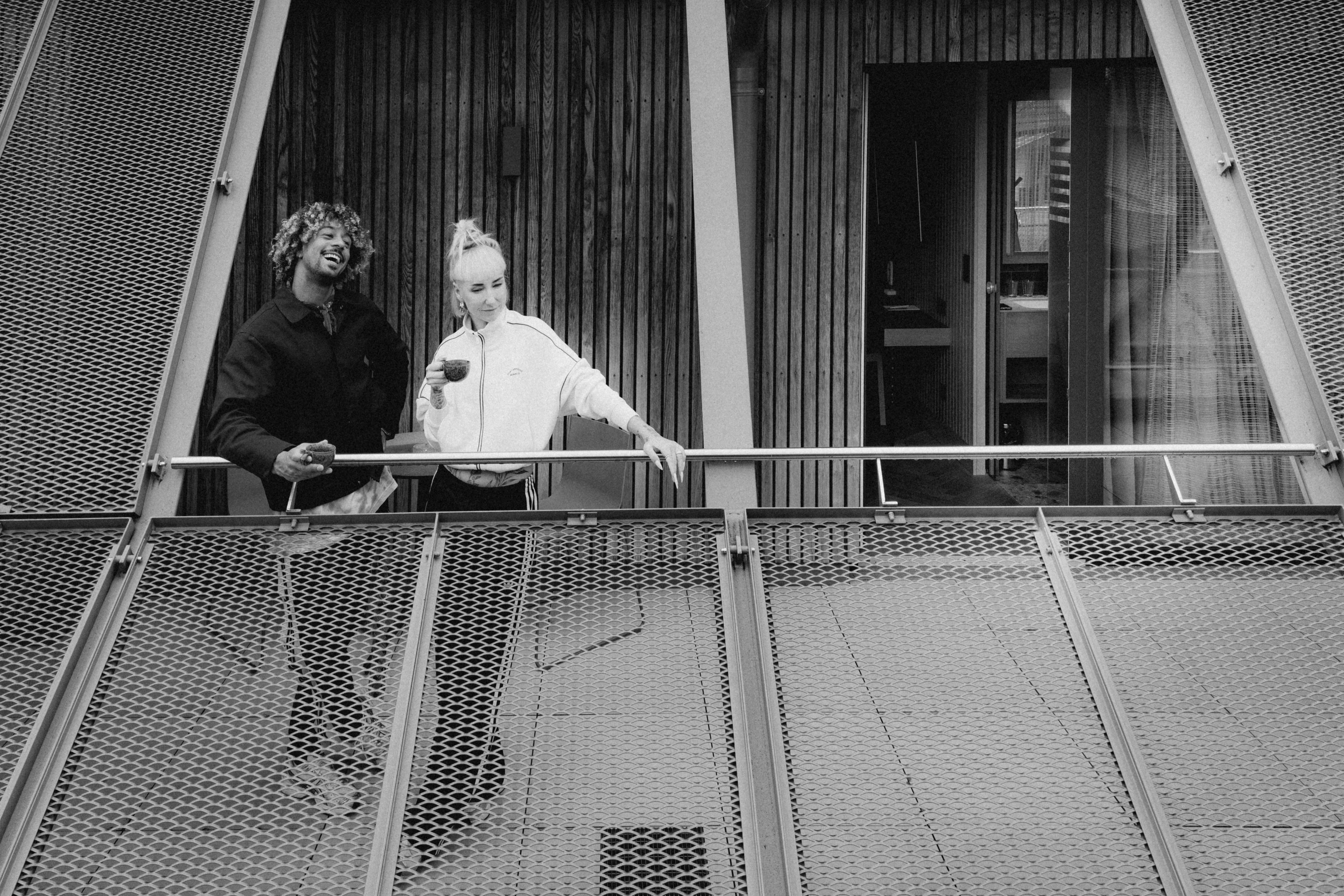 A cozy hotel room featuring a bed, lamp, and curtains in black and white tones.