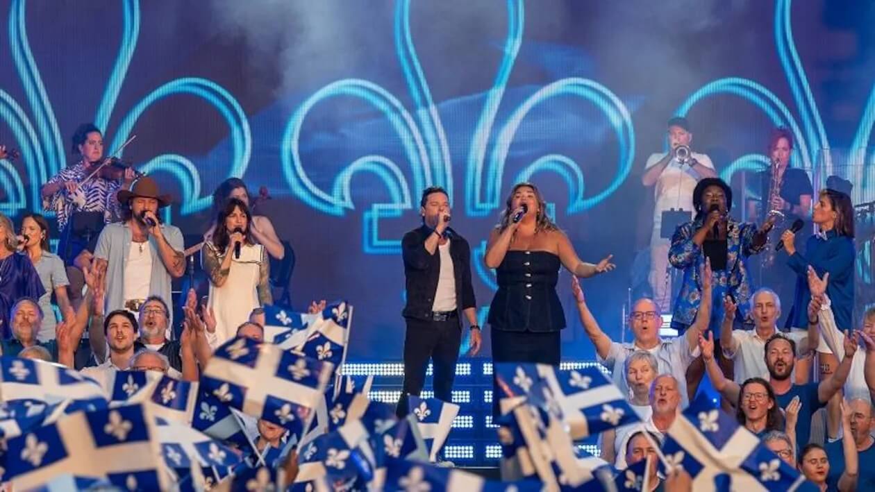 Elisabeth St-Gelais chante avec plusieurs artistes lors d’un grand spectacle de la Fête nationale devant une foule brandissant des drapeaux du Québec.