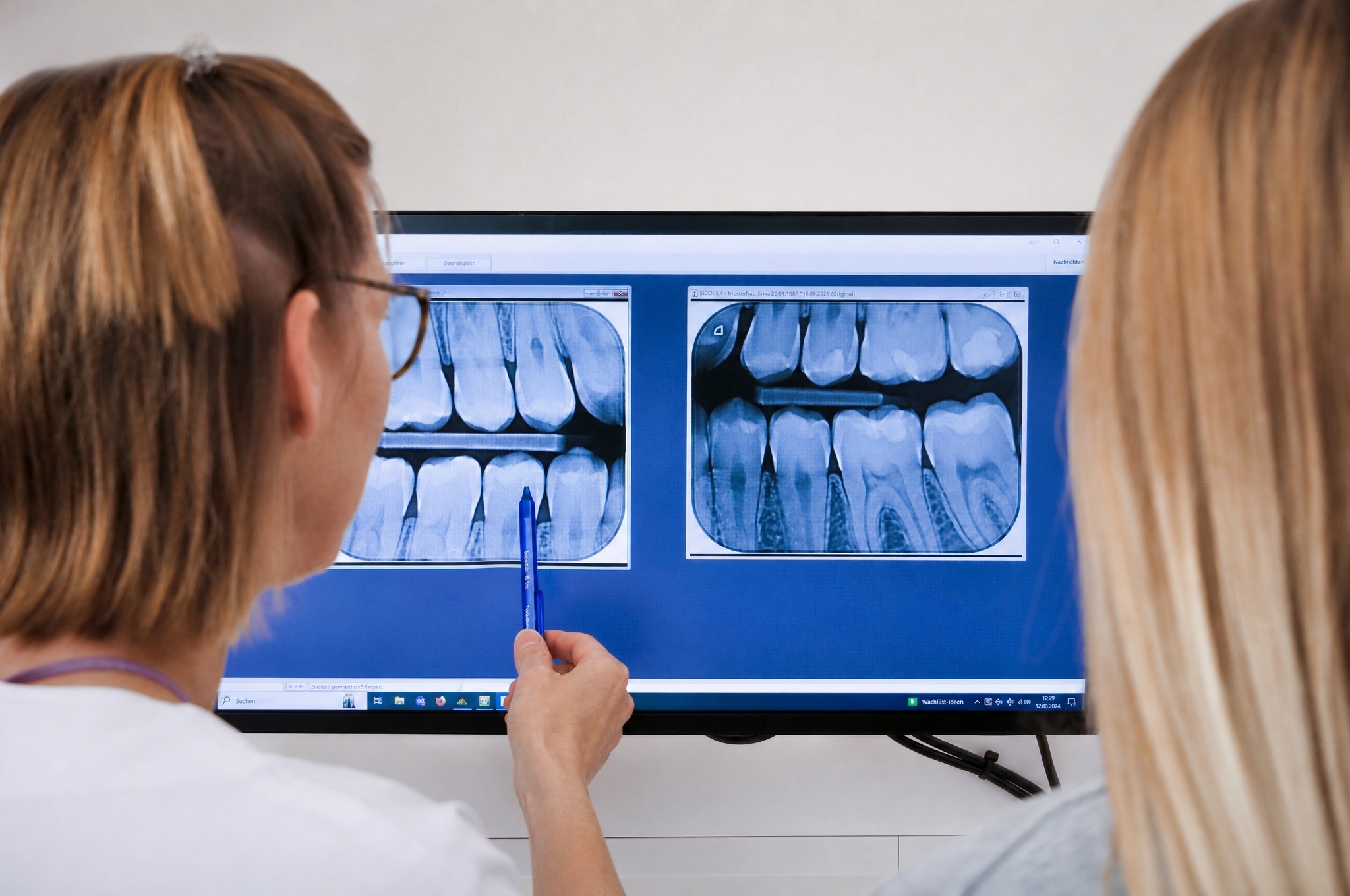 An over-the-shoulder view of two people analyzing digital blue-toned dental X-ray images on a computer monitor.