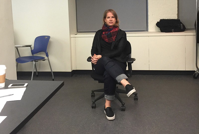 A photo of a woman siting on a chair in an office.