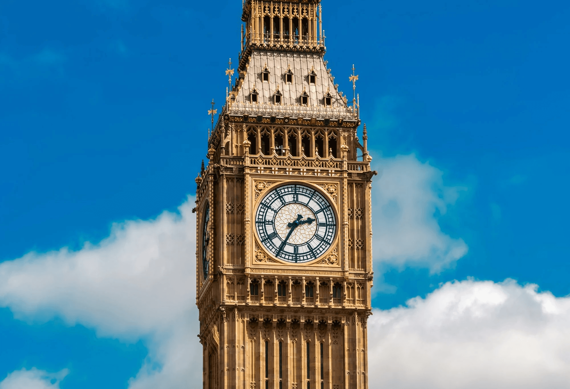 Close-up view of Big Ben clock tower in London under a bright blue sky with white clouds, symbolizing British culture and English language learning inspiration.