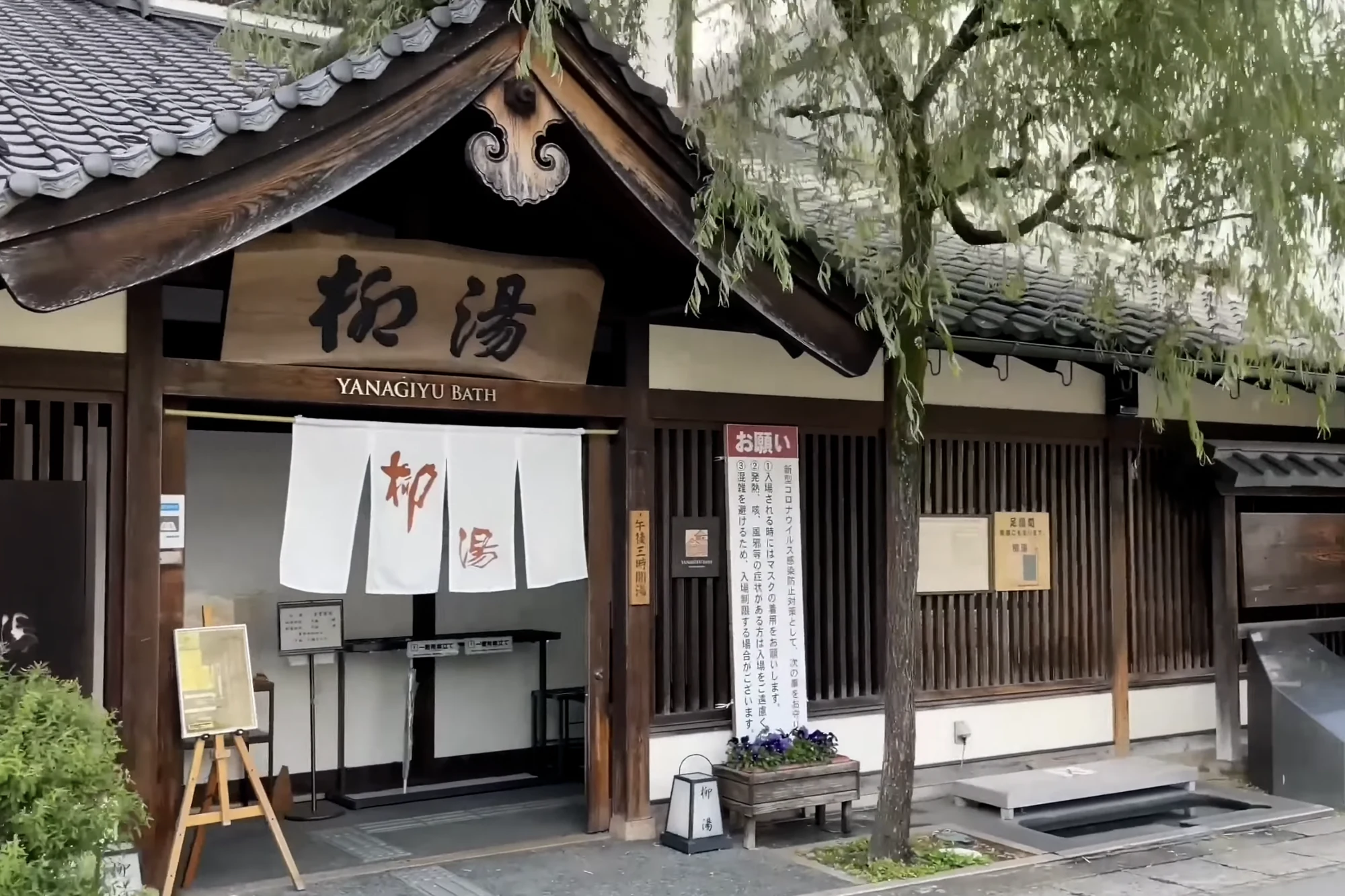 The timber facade of Yanagi-yu bathhouse in Kinosaki under summer green.