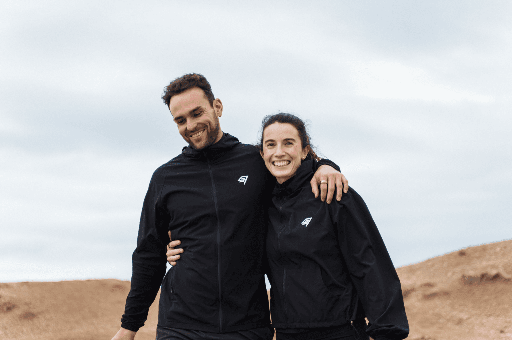 Dynamic close-up of a runner’s foot mid-stride on a muddy forest trail, wearing black socks and red trail shoes with visible sole pattern.