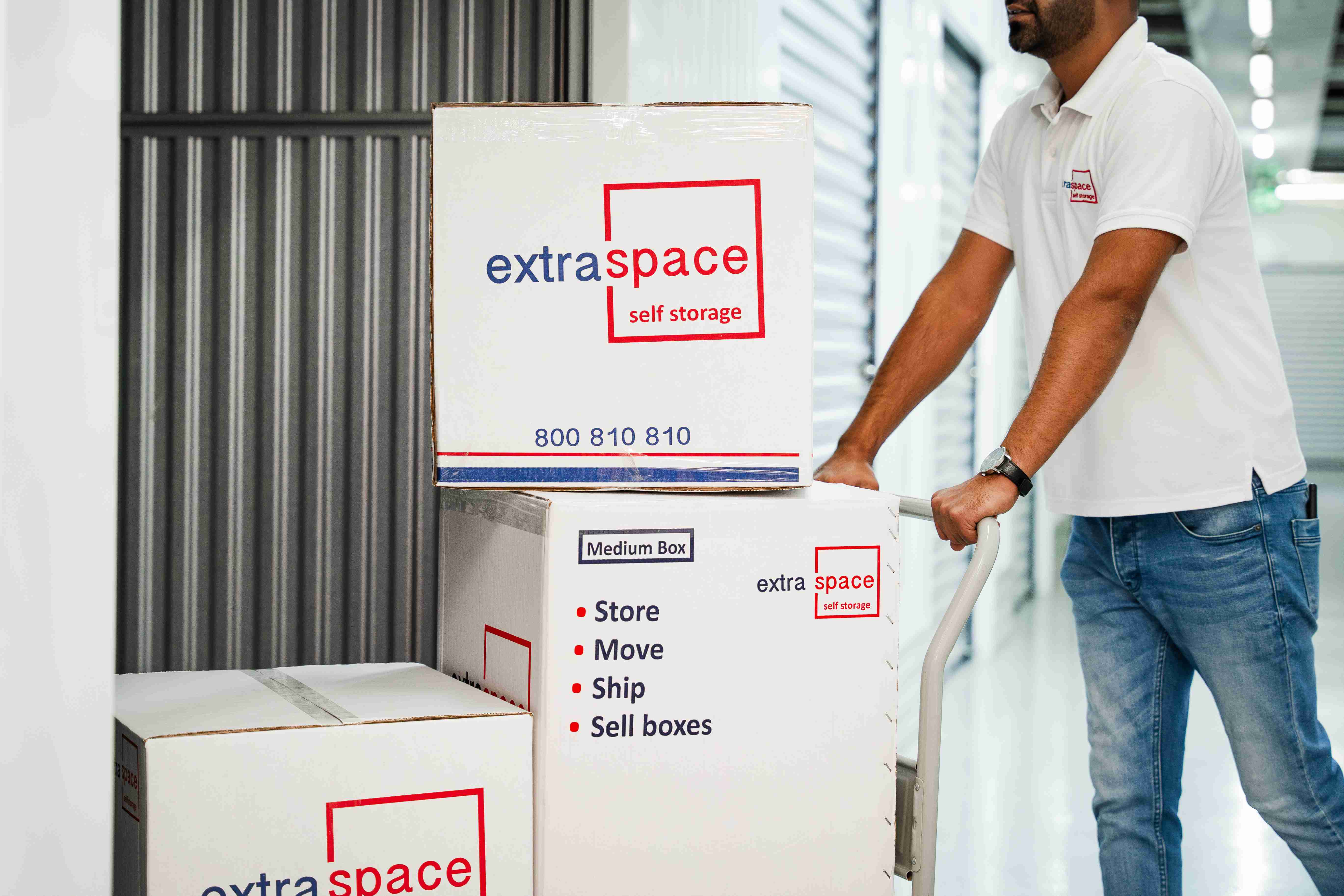 Warehouse worker transporting self-storage boxes on a trolley outside the facility.