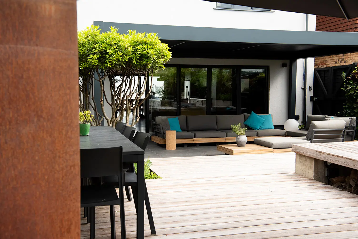 A modern outdoor space with patio seating, greenery, and a view of a stylish house.