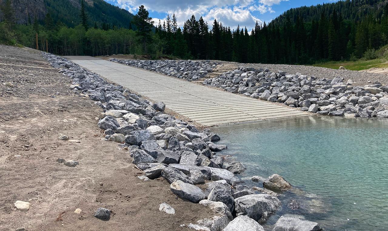 Excavator working on sediment removal at Barrier Lake with mountain backdrop in Kananaskis