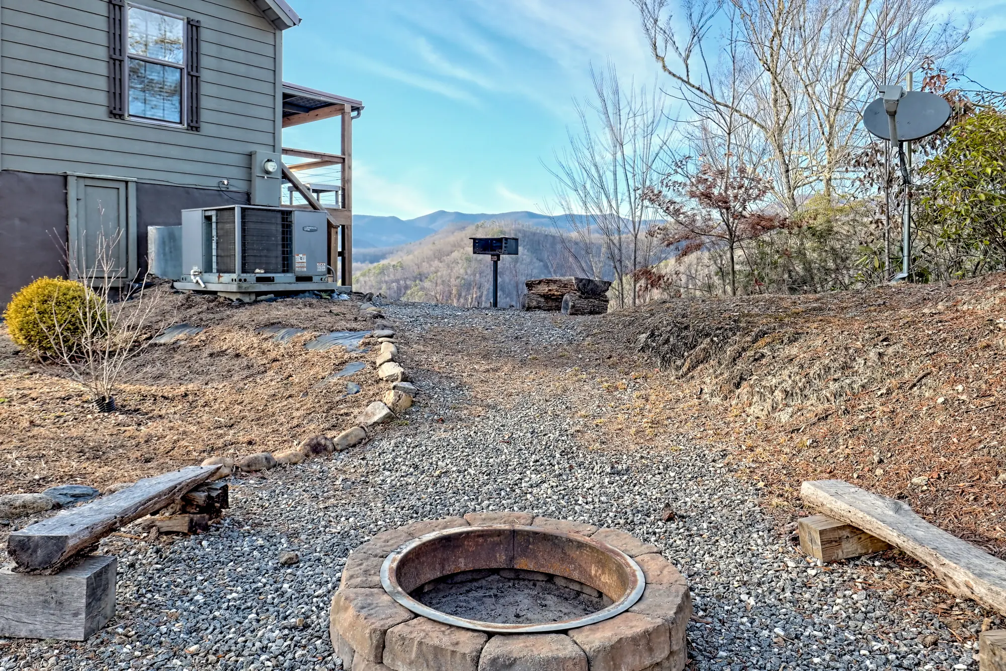 Gravel fire pit circle with log benches beside Tiny Tuck, mountains beyond