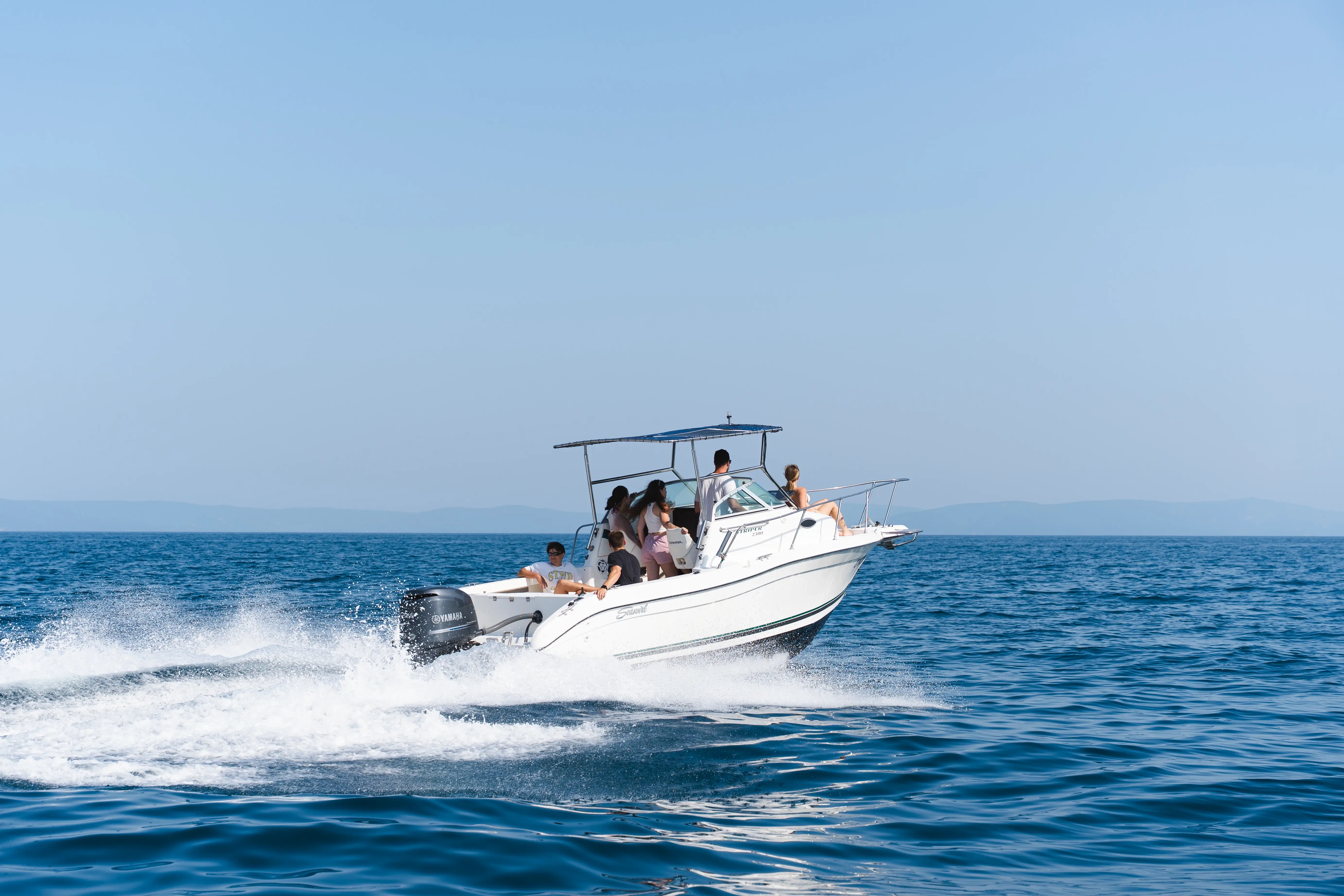 Speedboat cruising at high speed on the Adriatic Sea with a group of friends enjoying a sunny day on clear blue water.