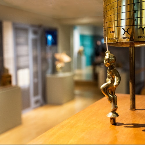 黃銅雕像特寫:一個小人物正攀爬柱竿,背景是模糊的歷史博物館展品。