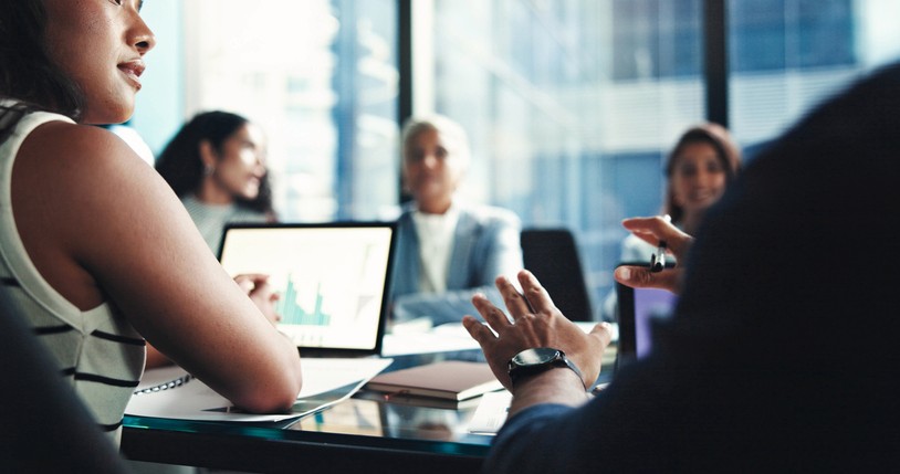 people sit around conference room table, talking, looking at computers