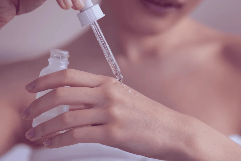 Close-up of a woman applying serum drops onto her hand using a dropper bottle
