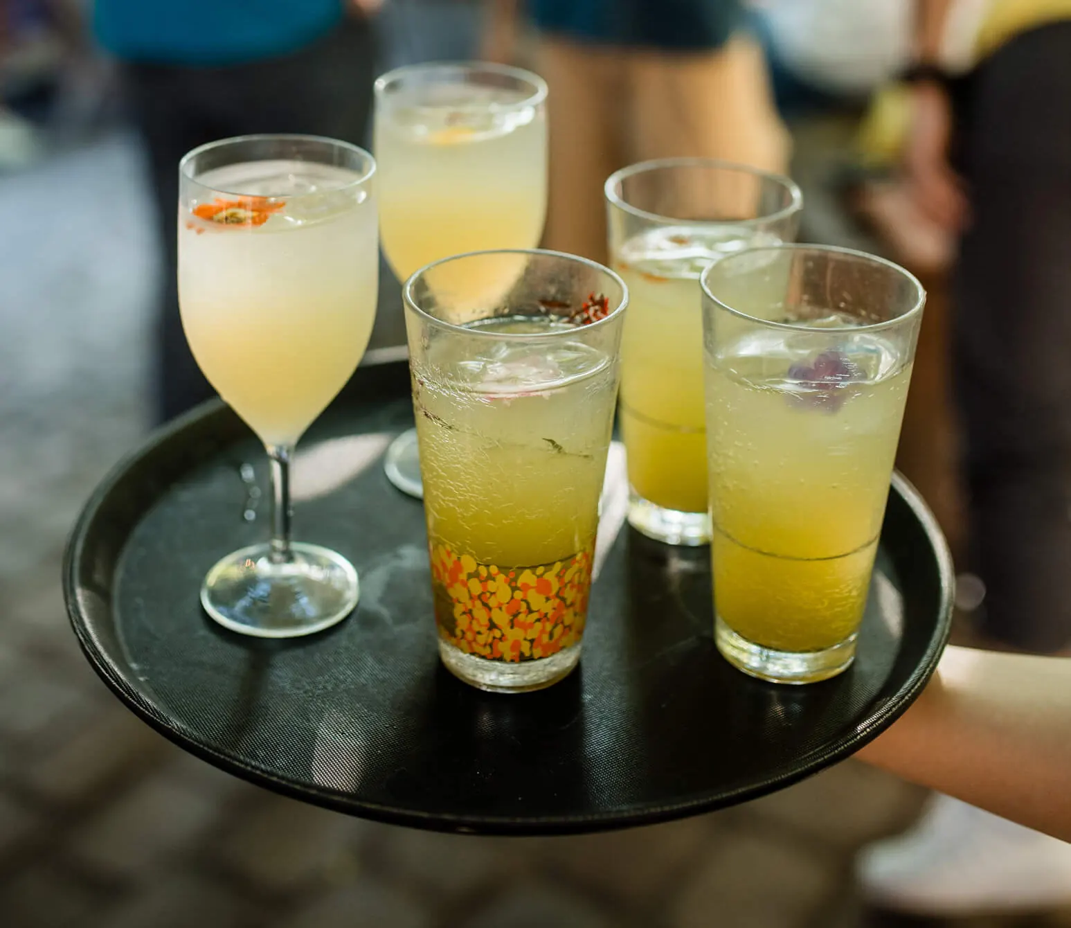 Servicekraft trägt ein Tablett mit Drinks durch den Garten
