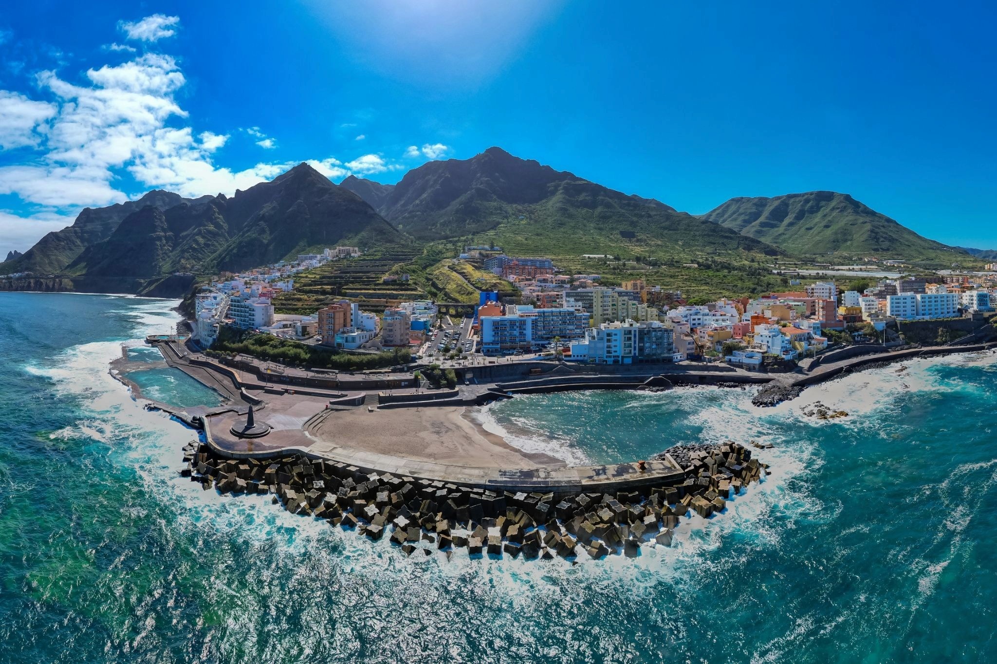 A shot from the sea of the coastline of Tenerife, with mountains in the background and the Bajamar pools on the left-hand side of the curving coastline