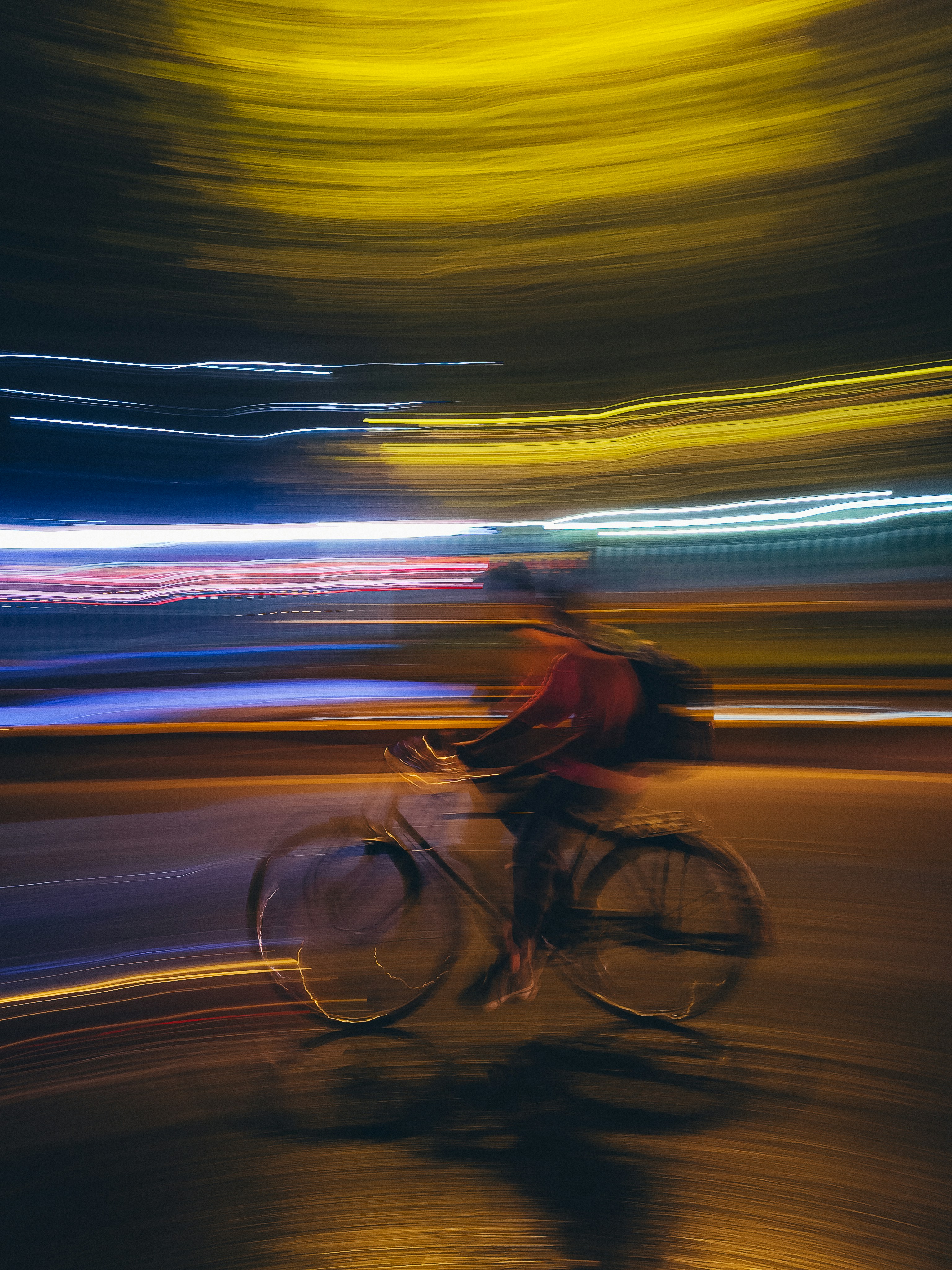 Cyclist blurred by motion at night with light streaks.