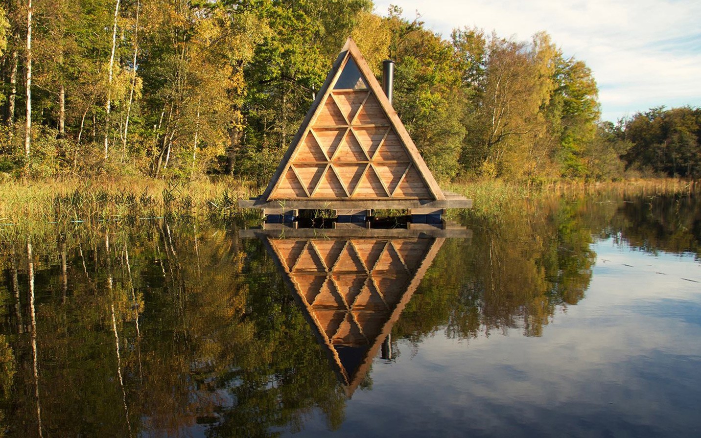 Floating Sauna with triangular timber facade reflected in forest lake designed by Asger Risborg Jakobsen