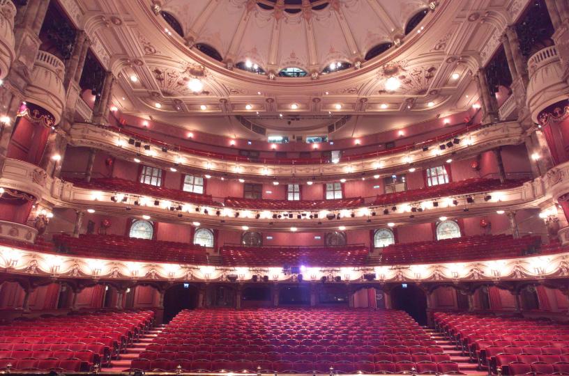 Grand interior of the London Coliseum with ornate balconies and red seating.