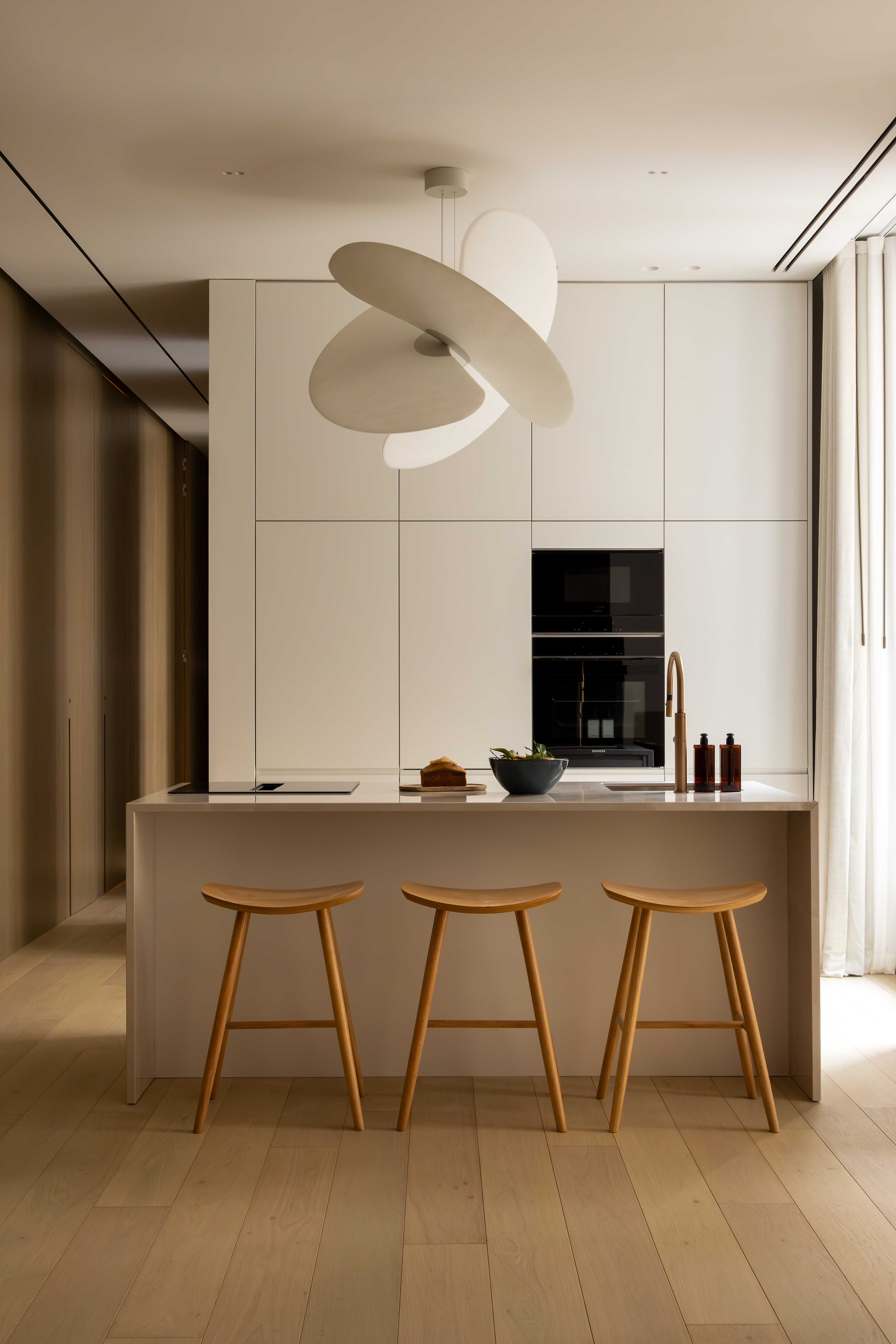 Cuisine ouverte avec ilot central, trois tabourets en bois, suspension sculptural blanche et placards integres