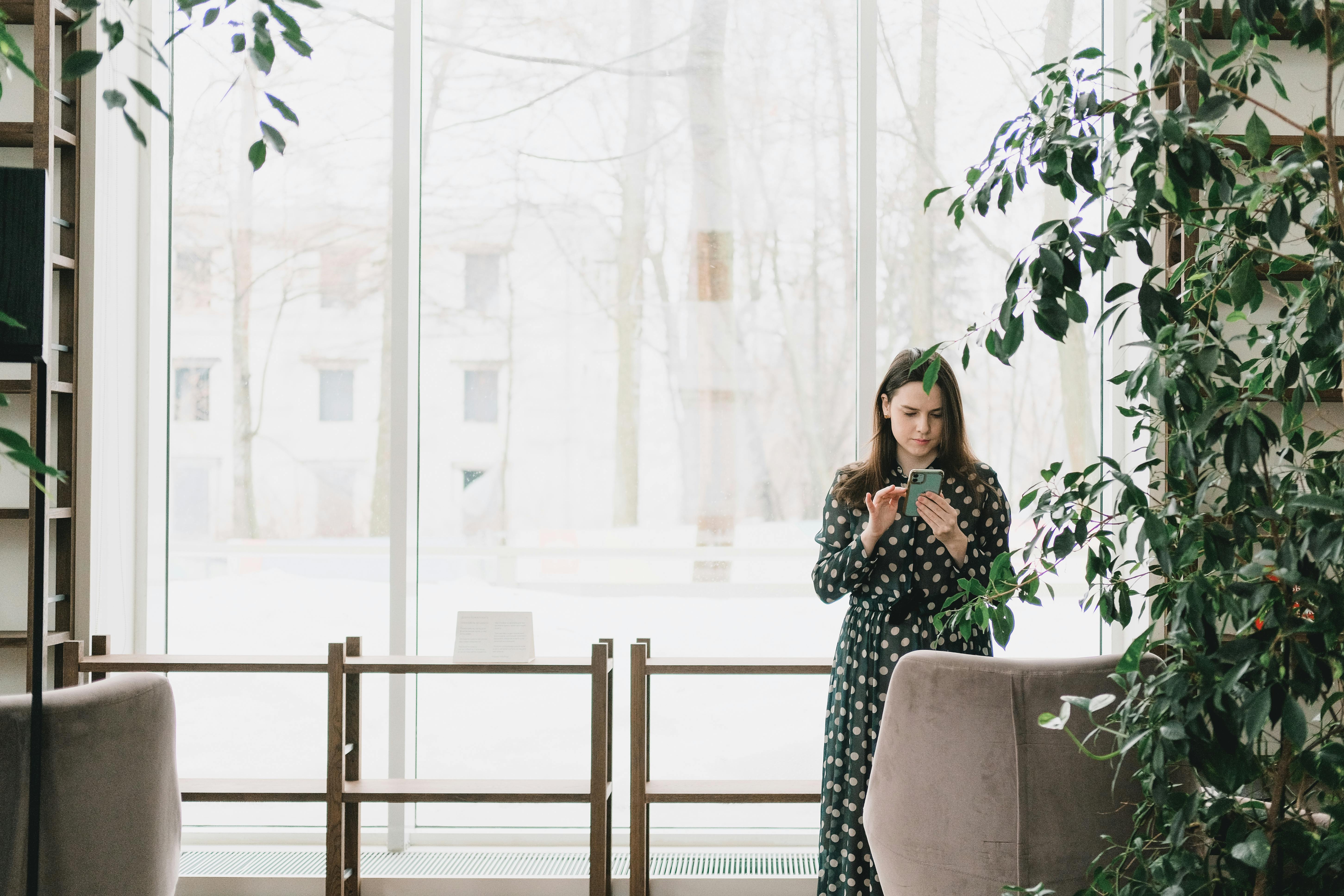 Focused young woman using smartphone near window in office