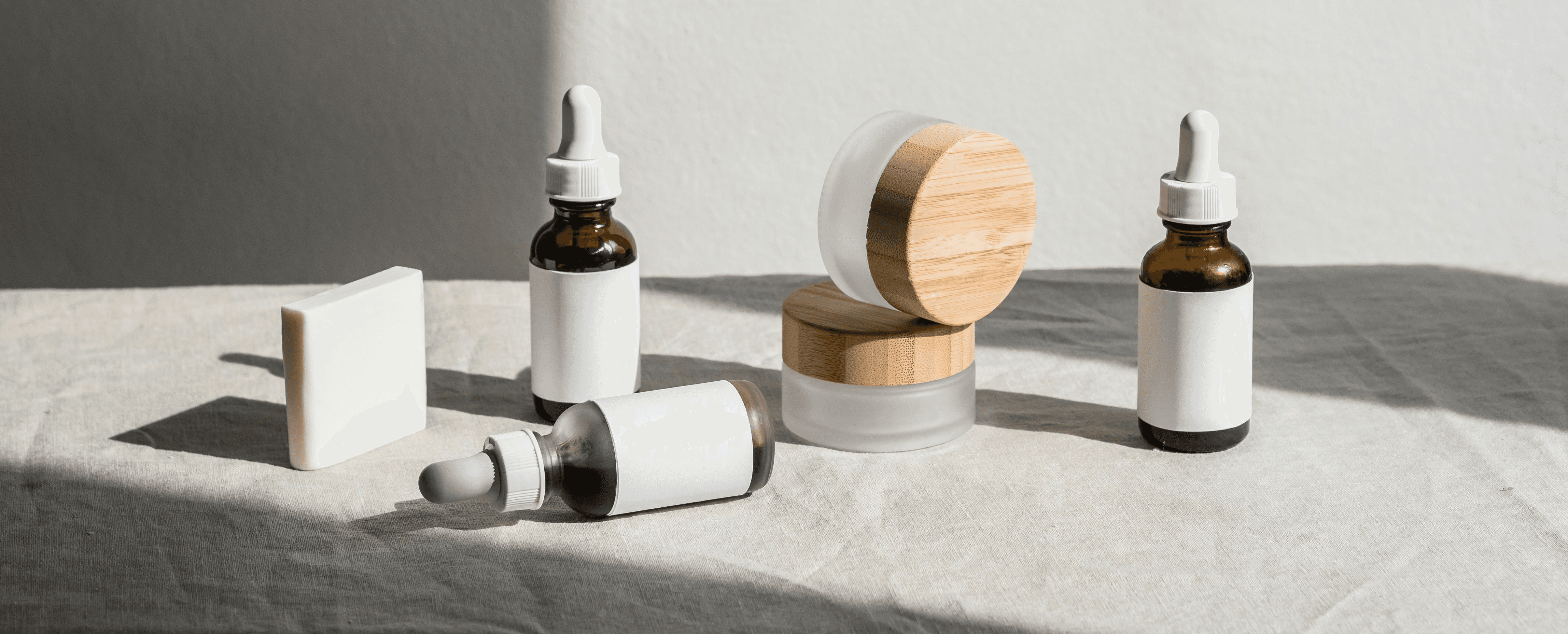 Spa products: skincare serum bottles, cream jars, and soap bar on white cloth. Natural beauty products, self-care concept.