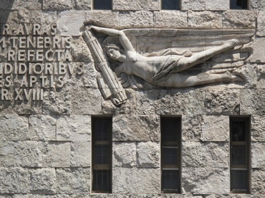 A wall with a stone engraving that depicts some letters and an angel with a fasce.