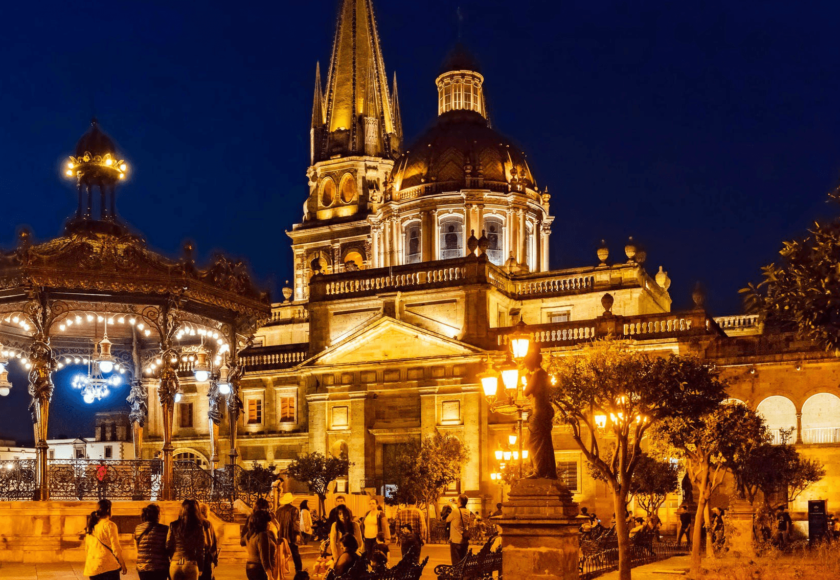 Outdoor restaurant terrace overlooking a tranquil lake at sunset. White tables and chairs are set with glassware. Sheer curtains add elegance. Calm ambiance.
