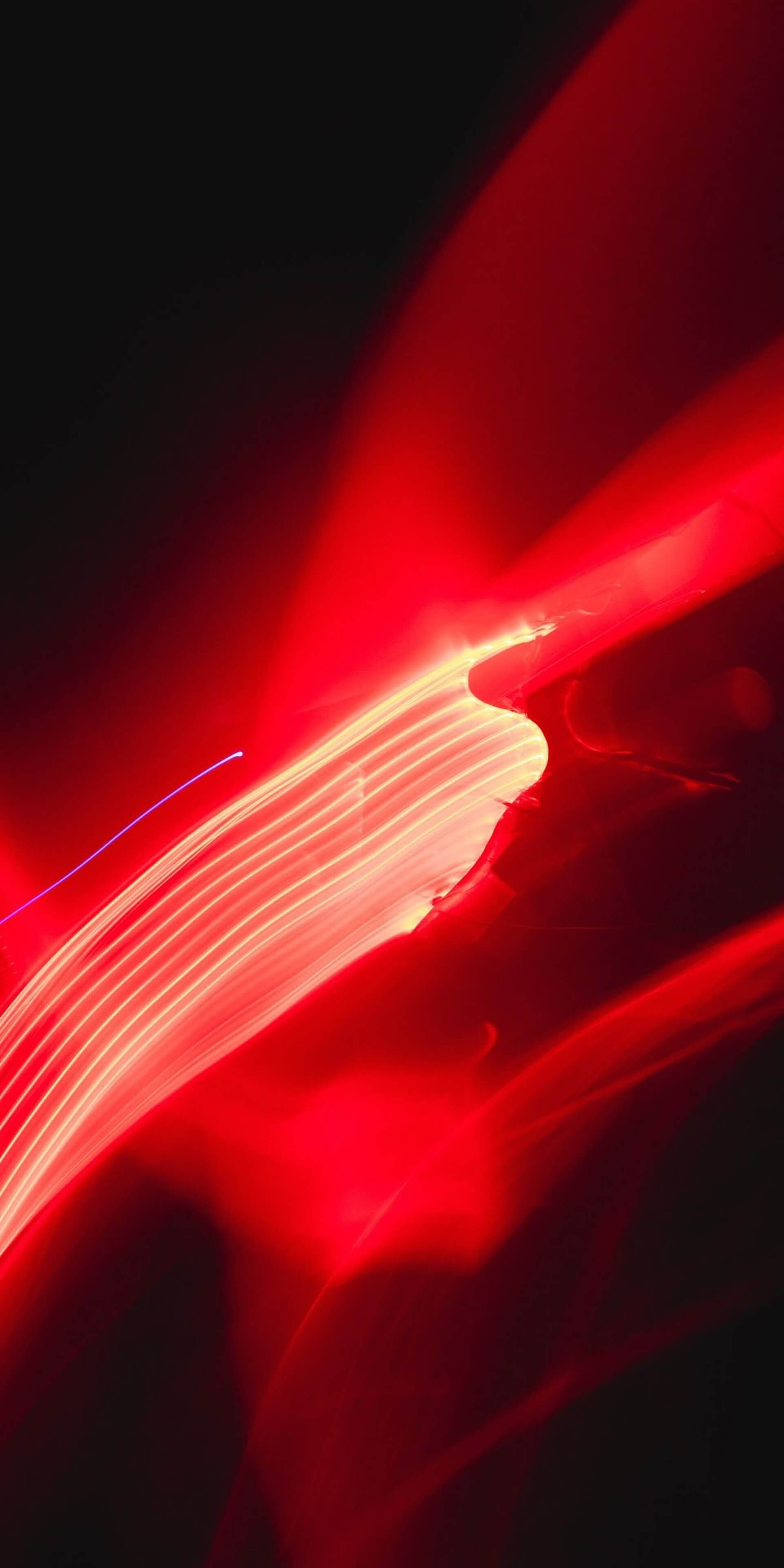 Abstract long-exposure photo featuring streaks of bright red and white light against a dark background. The dynamic curves and glowing effect create a sense of movement and energy, resembling light trails or neon motion blur.