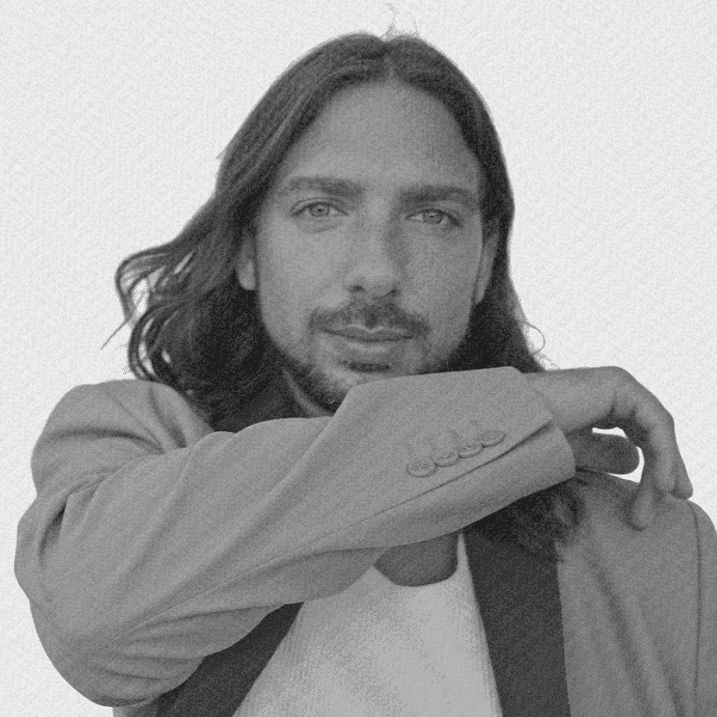 Portrait of a man with short dark hair and a trimmed beard, dressed in a dark shirt, on a simple background.
