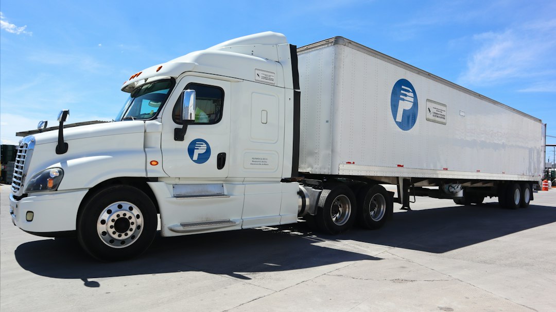 fleet of white delivery vans parked in parallel rows in a large logistics hub, drivers in blue uniforms interacting with handheld devices, bright overhead fluorescent lighting