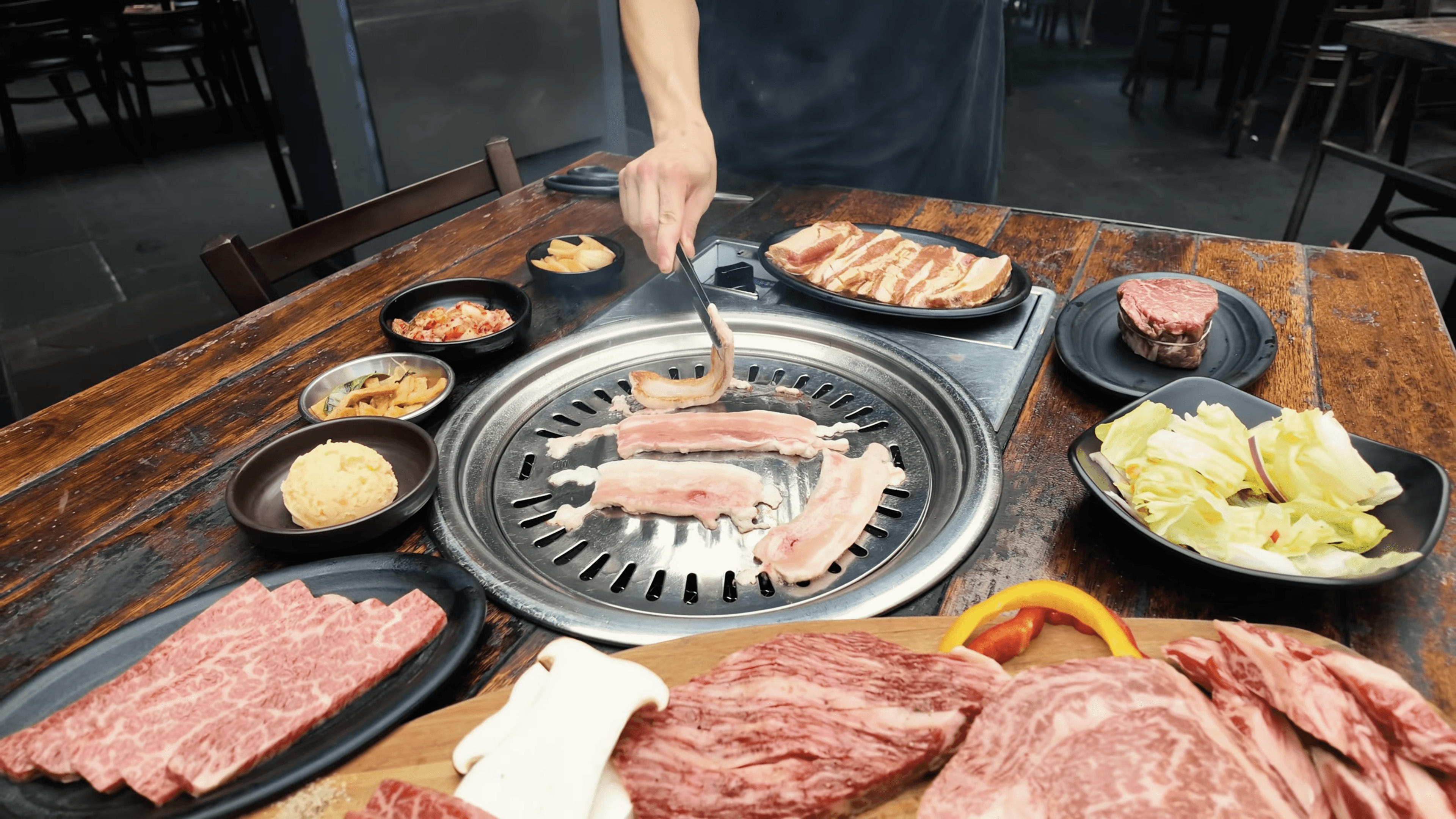 An overhead shot of Patatas Bravas or seasoned roasted potatoes, drizzled with a creamy white aioli sauce and sprinkled with chives, served on a dark gray plate alongside a small bowl of spicy red sauce.