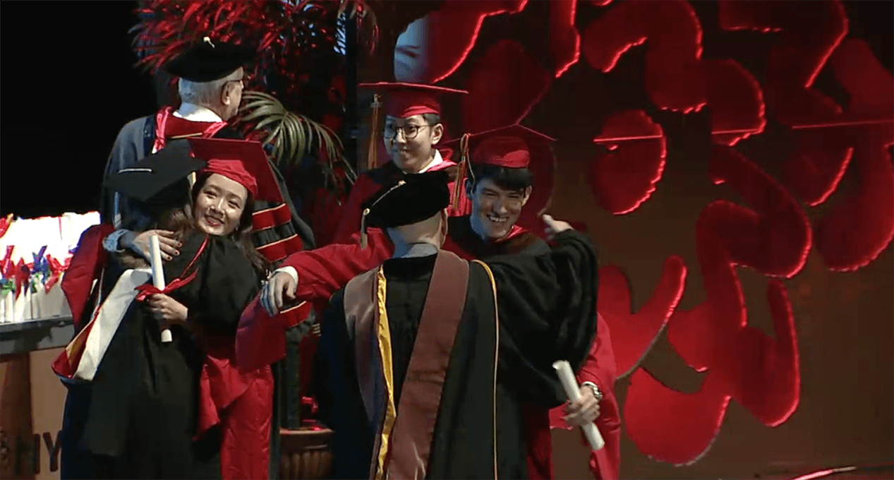 A photo of a couple of grad students and teachers, dressed in SVA color robes, that are hugging and congratulating each other.