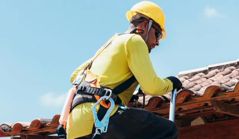 A climber in a yellow helmet and harness, focused on scaling a rocky surface against a blue sky.