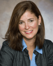Smiling woman with brown hair wearing a blue shirt and blazer. She is looking at the camera.