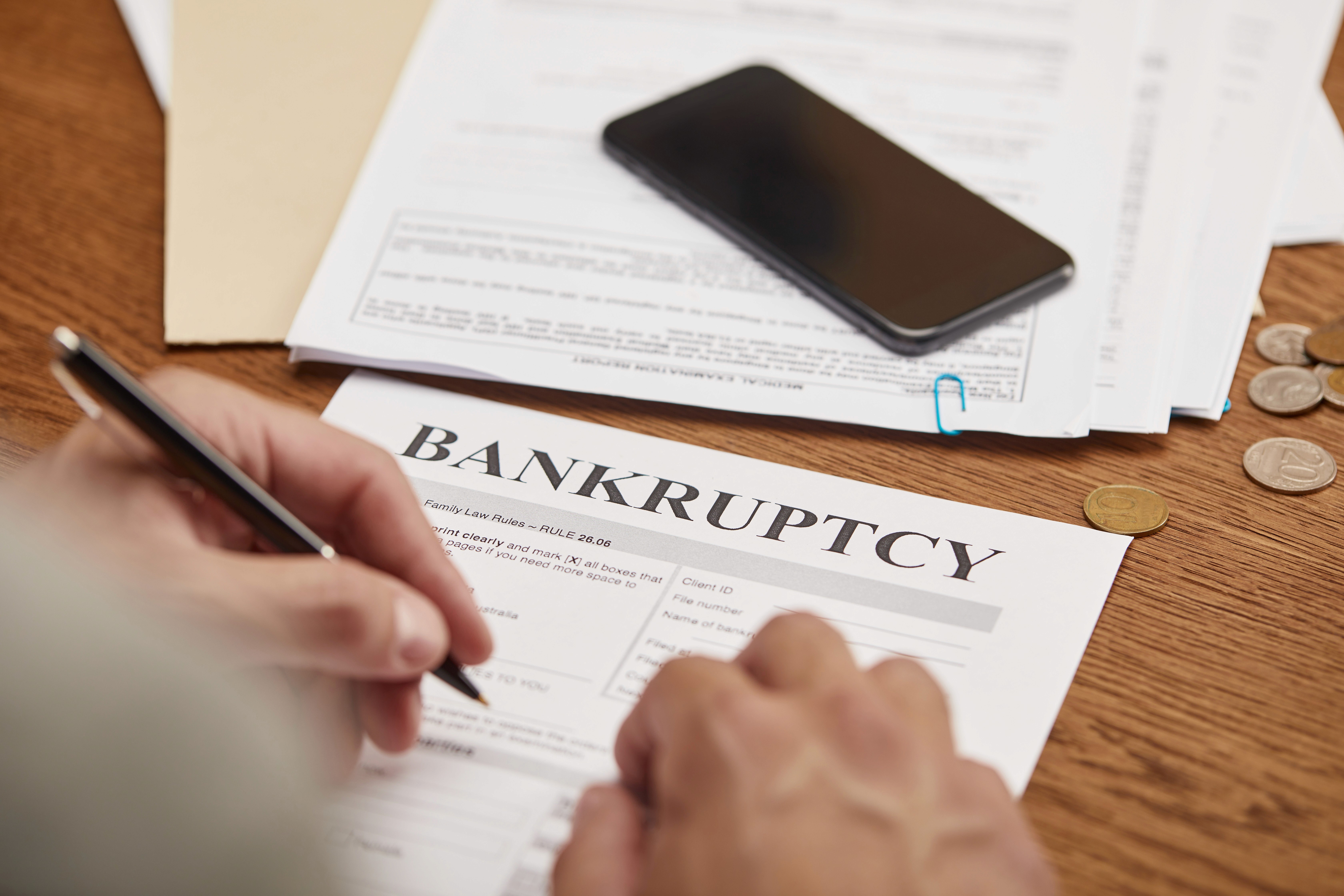 Person filling out a bankruptcy petition form with coins on the table, representing debt relief and fresh start bankruptcy filing at Lamb & Lamb, P.C. serving Essex County and the North Shore