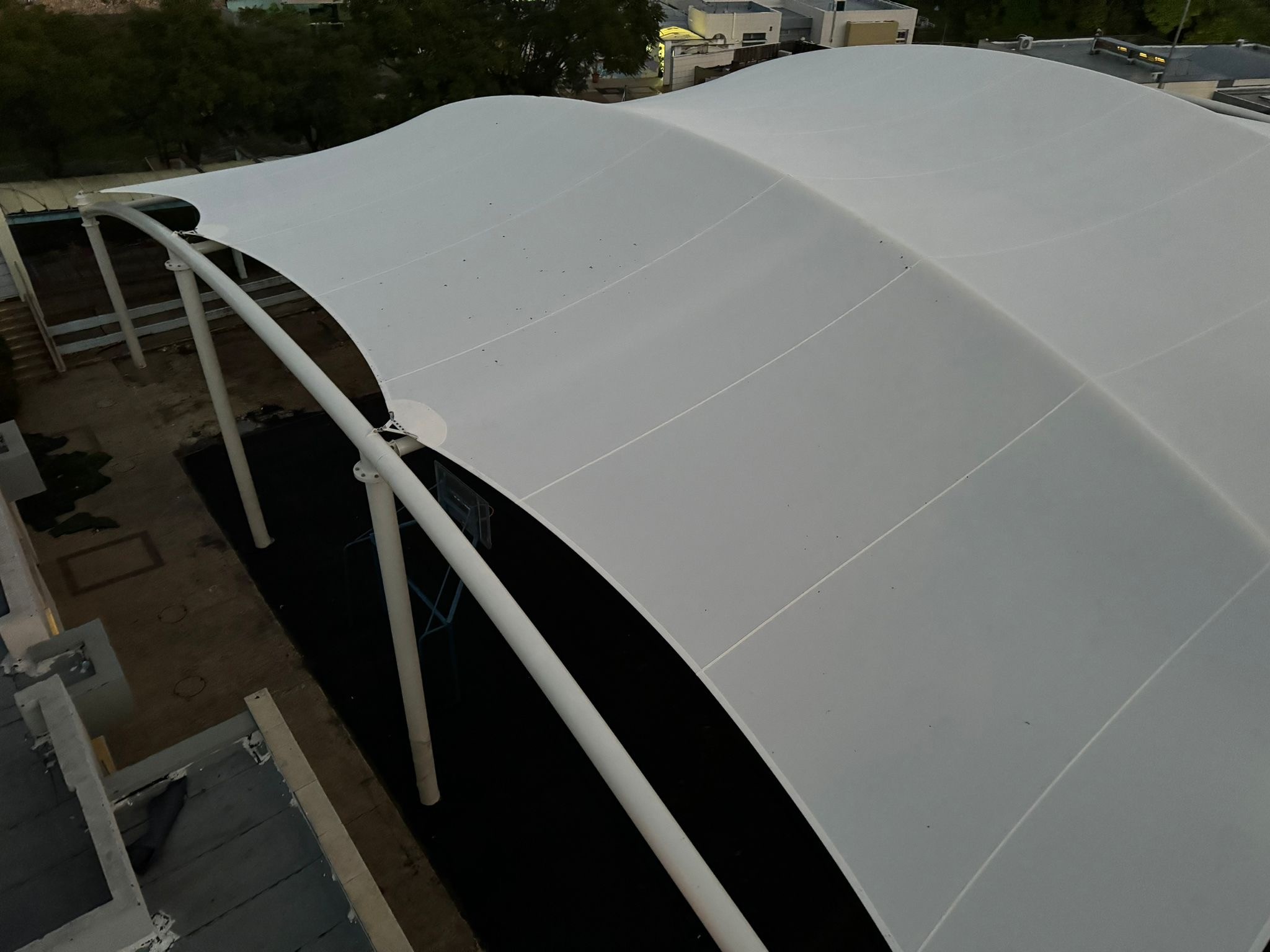 Top view on a large beige curved canopy supported by multiple pillars in an outdoor area.