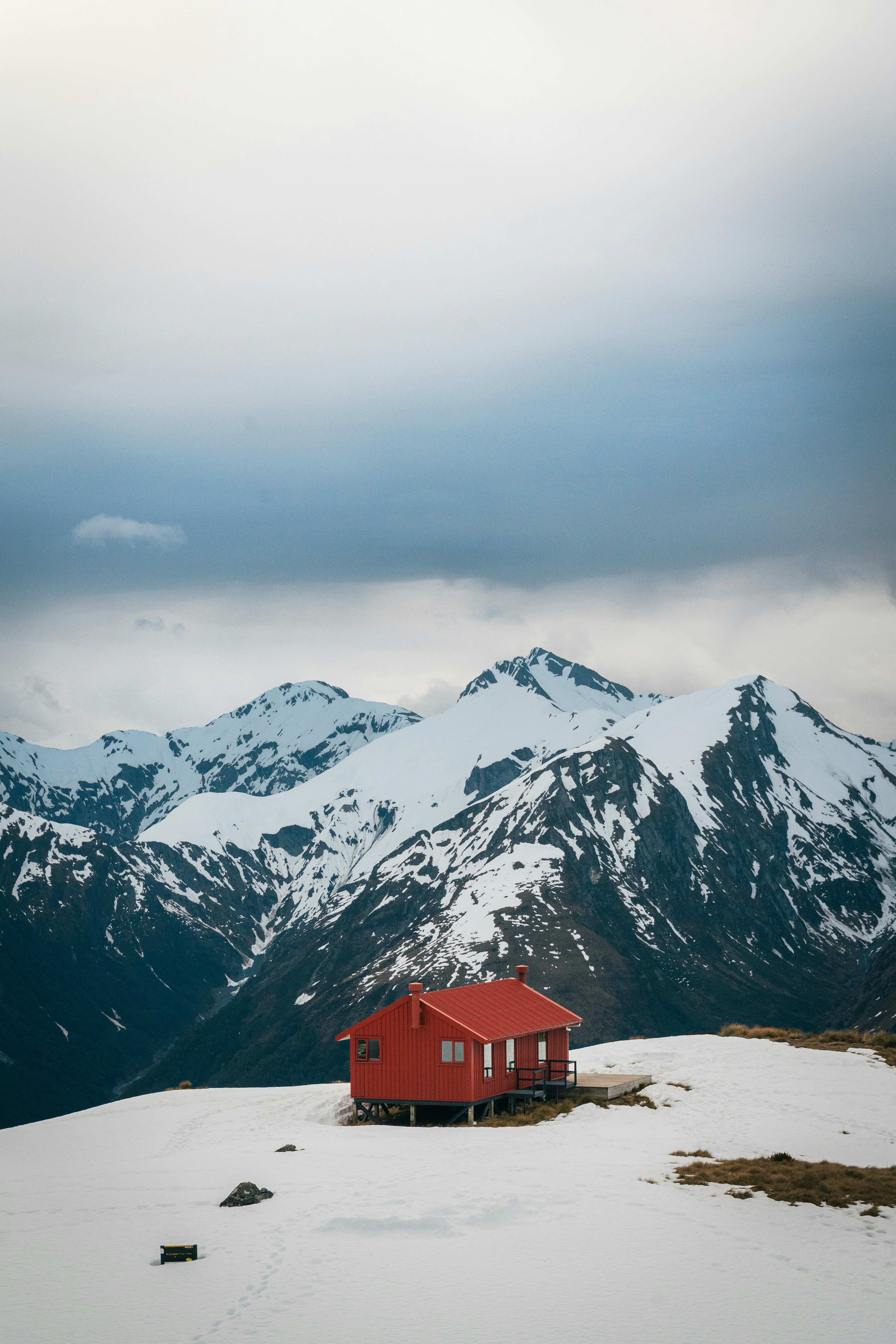 Red cabin sits on snowy mountain under cloudy sky
