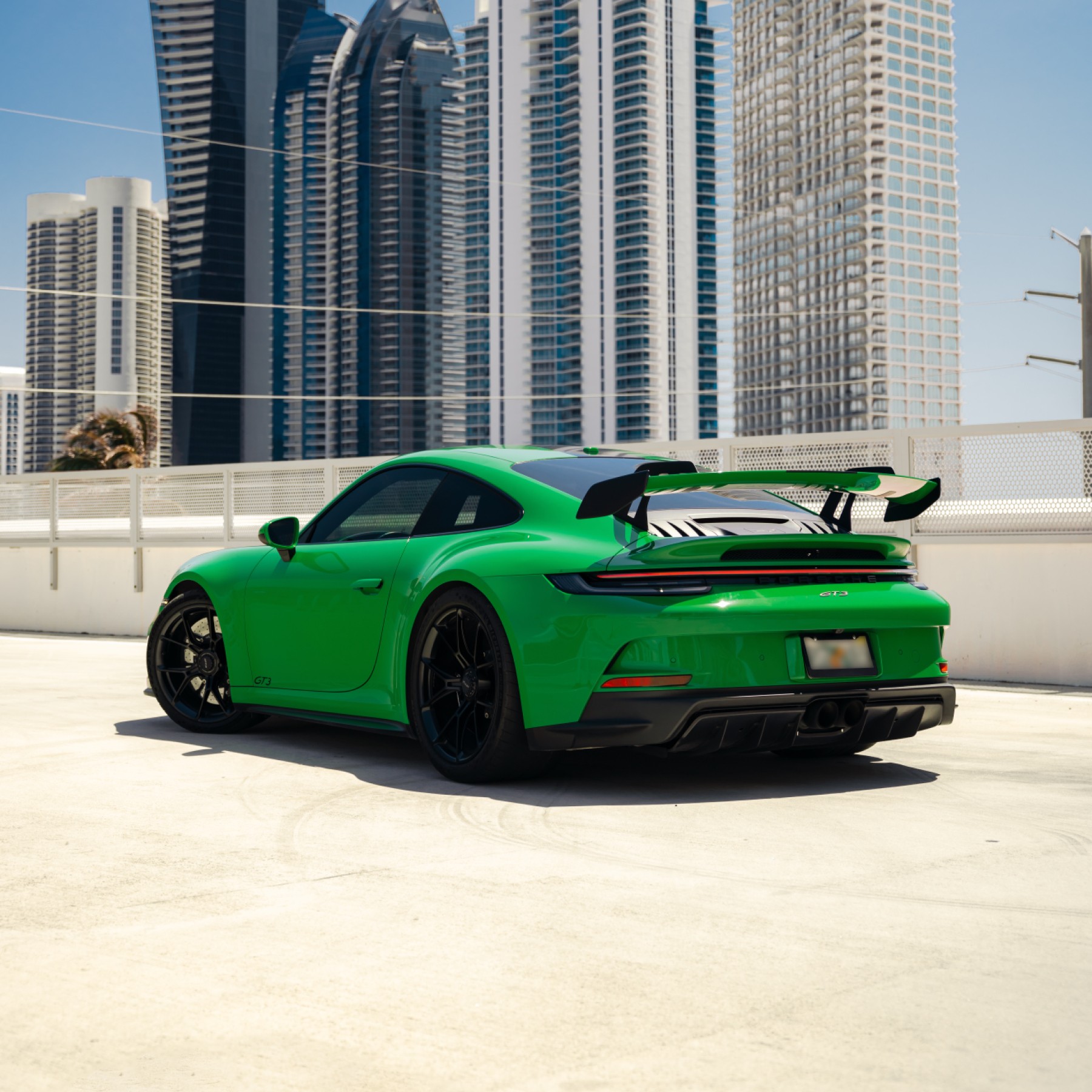 Rear 3/4 view of a green Porsche 911 GT3, highlighting its prominent rear wing and dual exhaust pipes, iconic for performance.