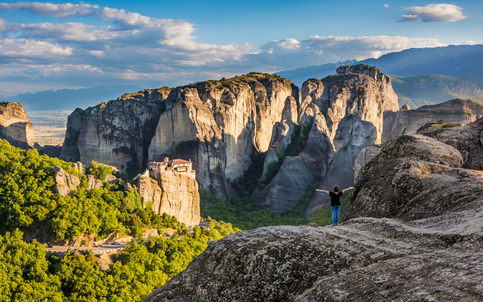 Meteora rock formations with monastery, person standing on cliff, Greece.